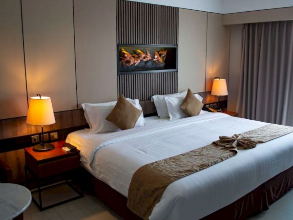 The image shows a tidy hotel room with a large bed, two side tables with lamps, and some decorations on the wall, creating a cozy ambiance.