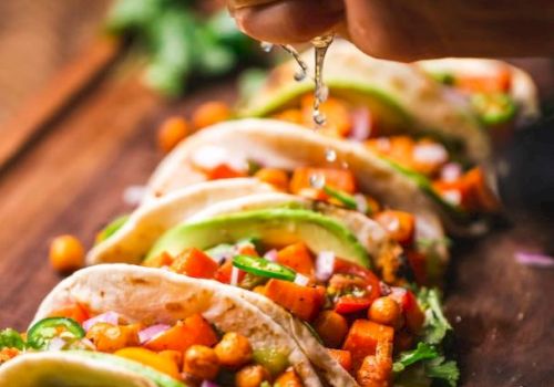 The image shows several tacos filled with chickpeas and vegetables, with a hand squeezing lime juice over them.