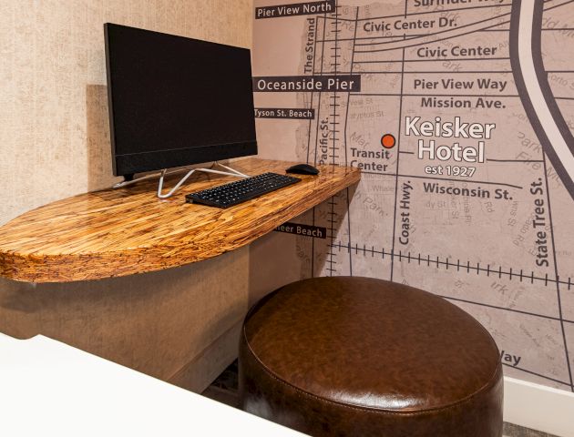 A small desk setup with a computer, keyboard, and mouse on a floating wooden desk. The wall features a map with 