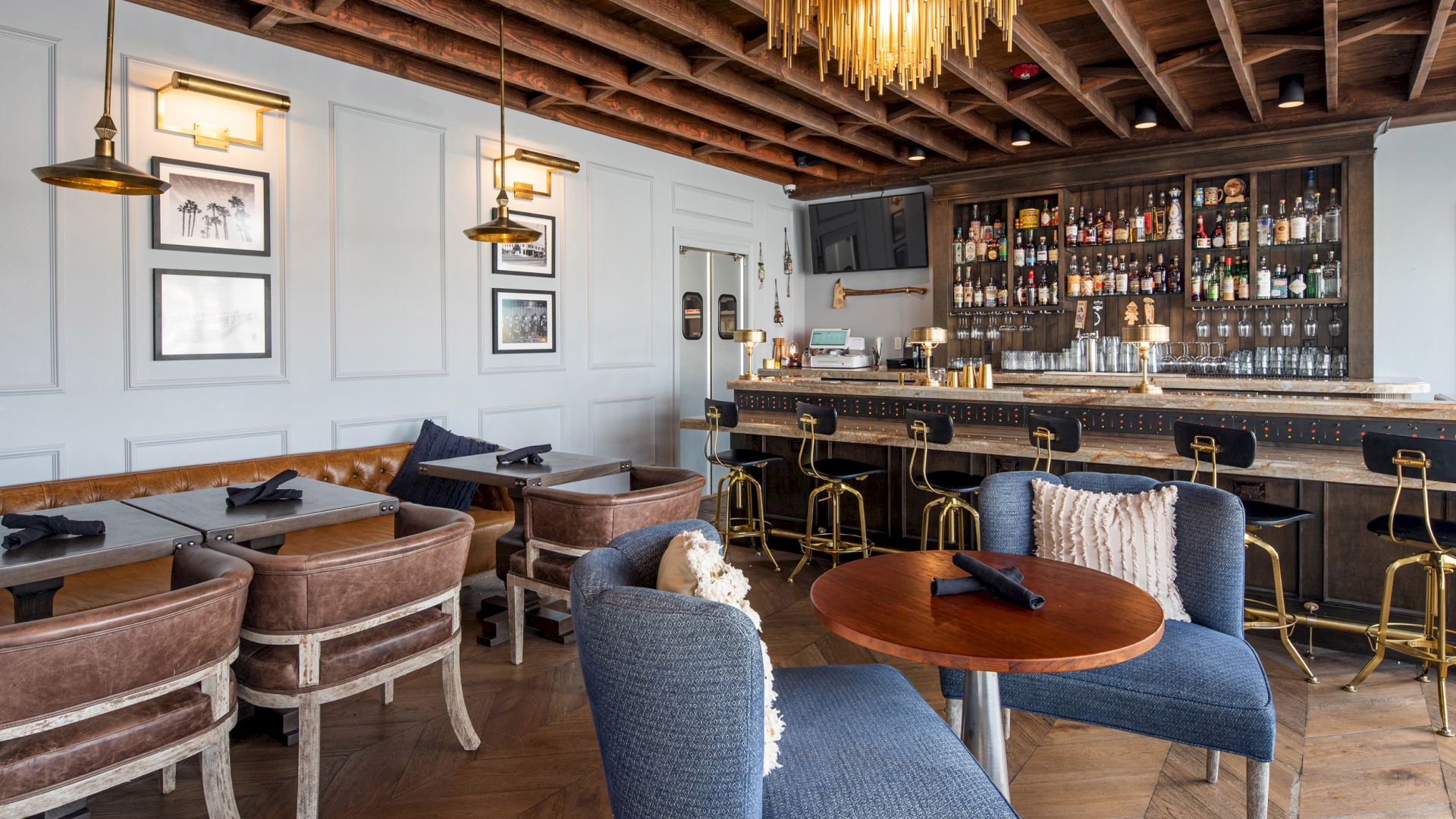 Cozy restaurant with modern decor, featuring a bar with stools, tables with chairs, framed pictures on the wall, and a stylish ceiling.