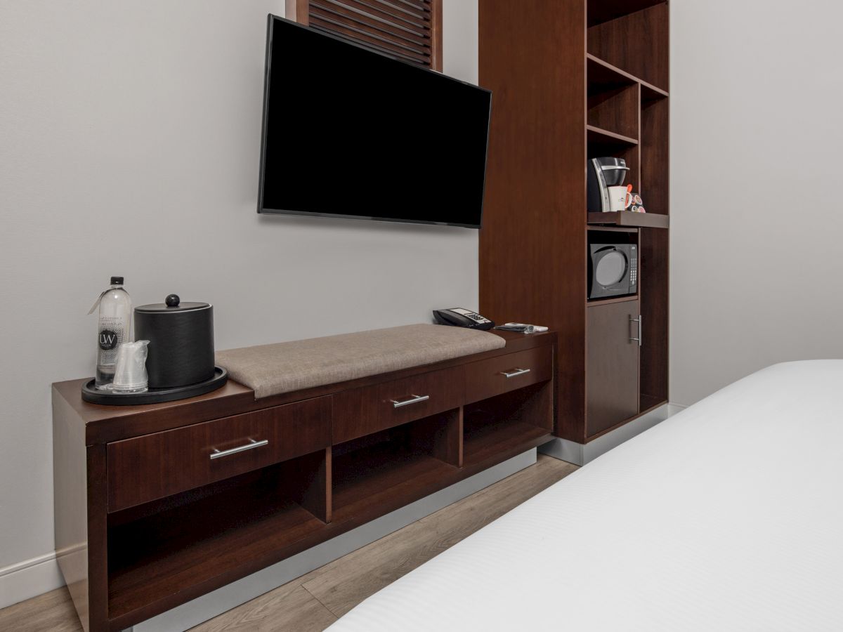 The image shows a hotel room setup with a wall-mounted TV, cabinet, water bottles, and an ice bucket.