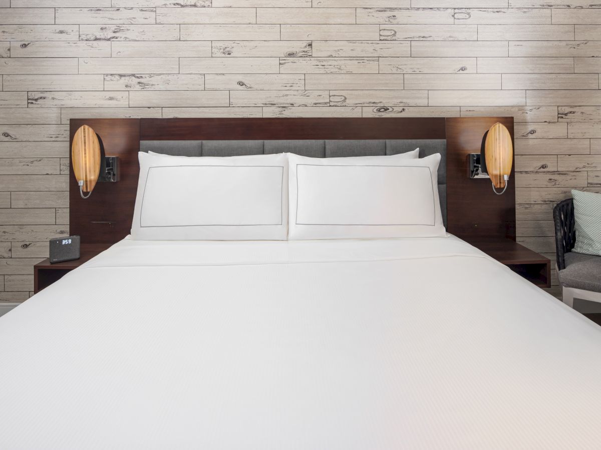 The image shows a neatly made bed with white linens, two pillows, and a headboard, flanked by two wall-mounted lamps in a modern bedroom.