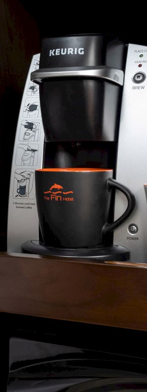 A Keurig coffee maker, two mugs, and a selection of coffee pods sit on a counter beside a modern desk lamp, ready for a coffee break.