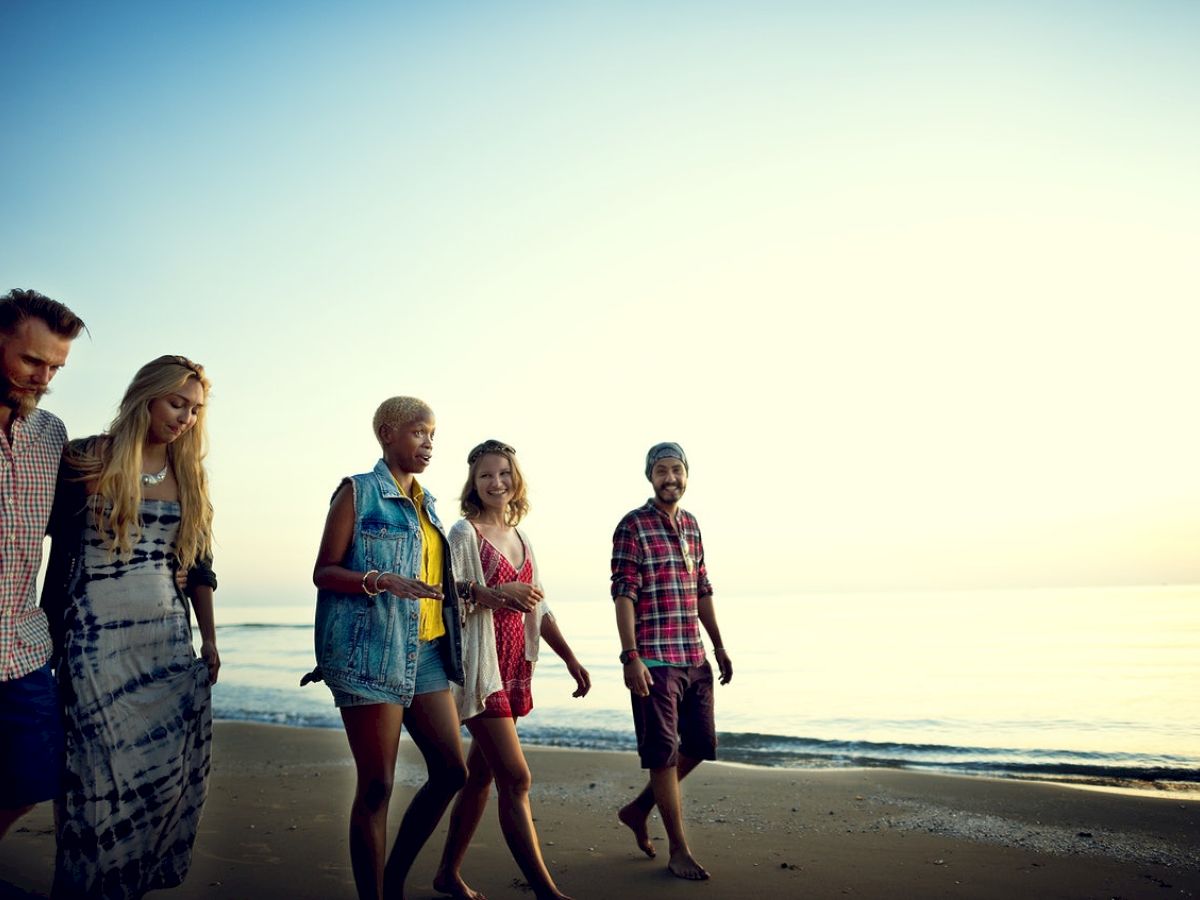 A group of five people walking along a beach at sunset, enjoying each other's company and the scenic view.