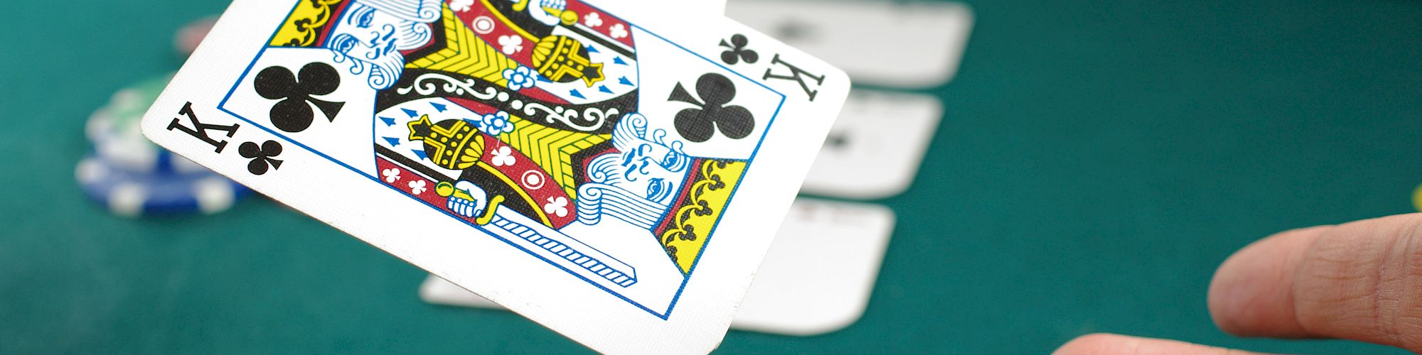 A person holding cards, including a king of clubs, on a casino table with poker chips and other cards visible in the background, ending the sentence.