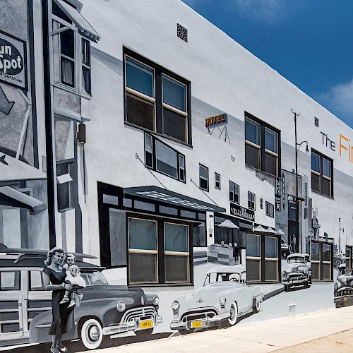 The image shows a building with a mural depicting a vintage street scene with classic cars and people from the mid-20th century.