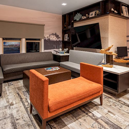 A modern office features a gray L-shaped couch, orange chair, and wood-patterned floor, with a large wall map and desk setup ending the sentence.