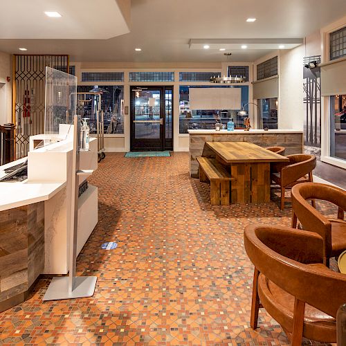 The image depicts a modern interior space with a reception desk, staircase, seating area, and a large table, all styled with warm, earthy tones.