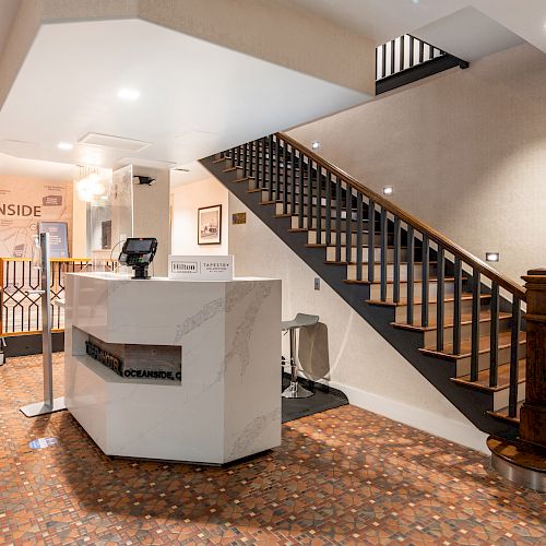 A hotel lobby with a check-in desk, staircase, and seating area with a sign saying 