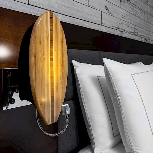 A modern bedroom scene featuring stylish wall-mounted wooden lights above white pillows and a dark headboard, with a textured wall in the background.