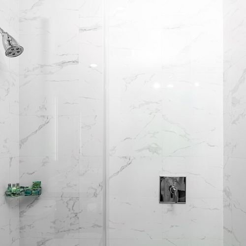 A modern shower with white marble tiles, a chrome shower head, and a built-in shelf holding toiletries. The shower has a glass door handle.