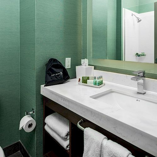 This image shows a modern bathroom with green walls, a sink, a mirror, toiletries, towels, and a toilet.