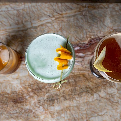 Three cocktails are on a marble surface. The drinks have different colors and garnishes, captured from a top view, ending the sentence.