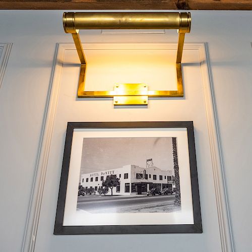 A framed black-and-white photo of a building, illuminated by a brass picture light, is mounted on a wall with decorative molding.