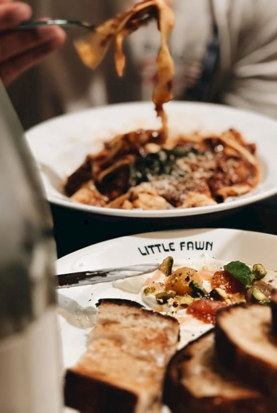 Two plates of pasta and toasted bread, fresh herbs, and a fork picking up noodles; a cozy, hearty meal moment ending with yum.